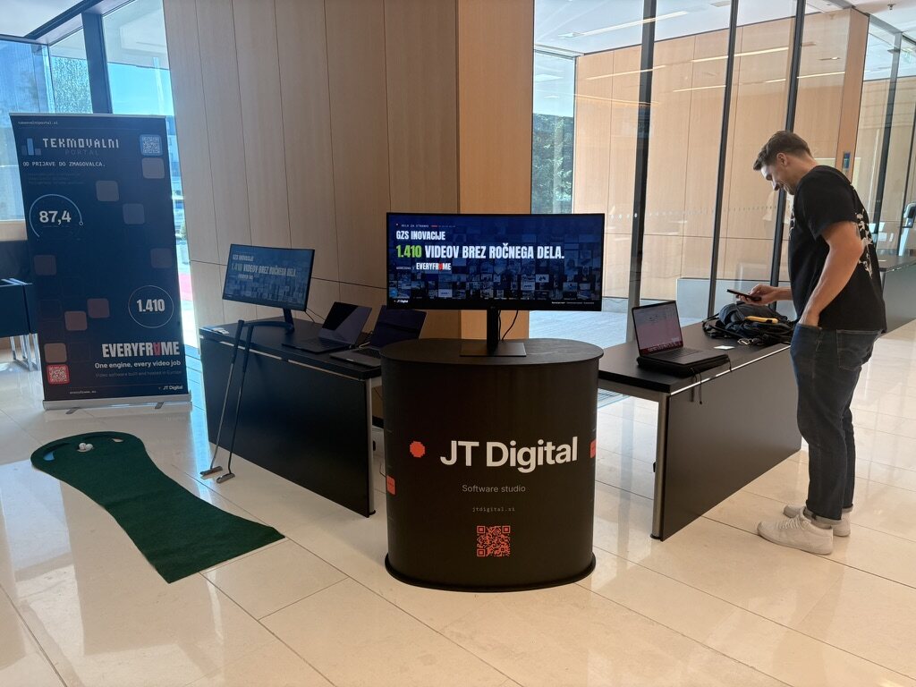 Our stand at Dan inovativnosti, with the JT Digital counter, a wide screen showing the GZS Inovacije part of our film, laptops and a putting green.